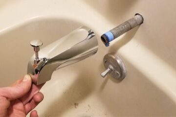 The image show a plumber fixing a dripping bathtub faucet.