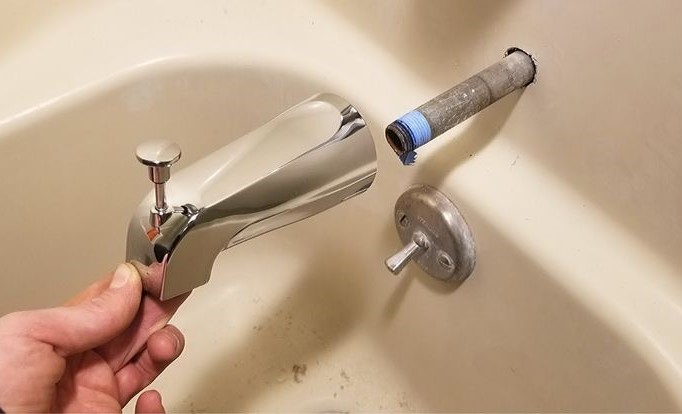 The image show a plumber fixing a dripping bathtub faucet.