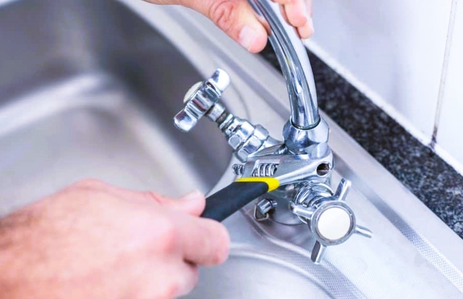 The image shows a man identifying and tightening the loose kitchen sink faucet.