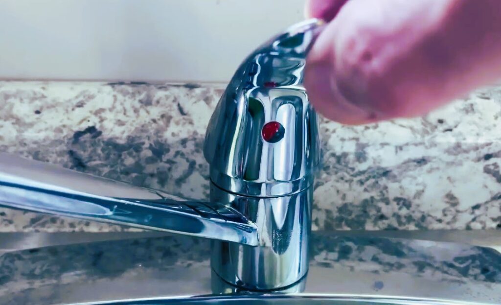 The image shows a man shut off the water from loose kitchen sink faucet.