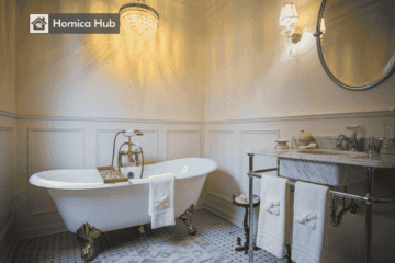 The image shows a vintage-style clawfoot bathtub with gold color feet, placed under a chandelier in an elegant bathroom with soft yellow lighting.